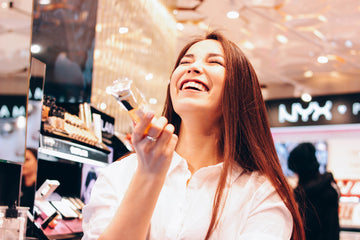 Woman Smiling While Holding Dossier Perfume Bottle in a Cosmetics Store