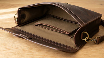 Close-up of a dark brown leather briefcase showing solid brass hardware, tight even stitching, burnished edges, and clean interior lining