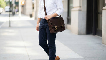 Person wearing a dark brown leather messenger bag crossbody with strap adjusted at hip level, showing correct carrying position for professional daily use