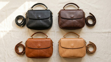 Overhead flat lay of four genuine leather bags in black, brown, cognac, and tan arranged on a cream linen surface