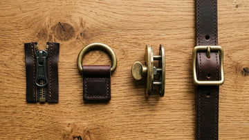  Close-up flat-lay of leather bag hardware components including a YKK zipper, brass D-ring, and turnlock clasp