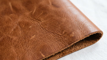 Infographic comparing full-grain, top-grain, and genuine leather across durability, patina, breathability, and price