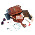 Open Brown Leather Saddle Purse Showing Spacious Interior, Surrounded by Sunglasses, Phone, Notebook, Makeup, and Earphones