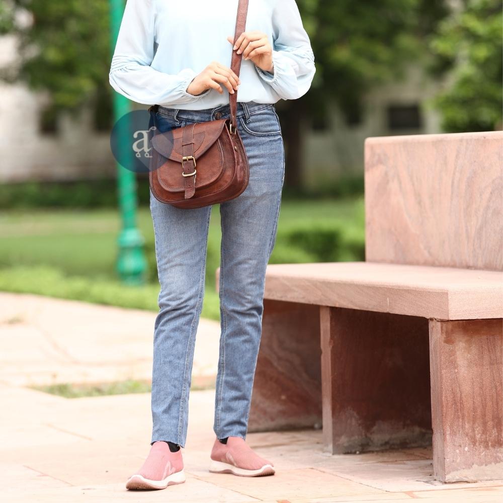 Woman in Casual Outfit with Blue Blouse and Jeans, Carrying Anuent's Brown Leather Saddle Purse with Adjustable Strap