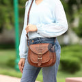 Woman Wearing Casual Outfit with Blue Blouse and Jeans, Showcasing a Brown Leather Saddle Purse with Buckle Detail