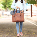 Woman Walking on a Leaf-Covered Path Carrying the Leather Laptop Tote Bag with Brass Buckles and Front Pocket