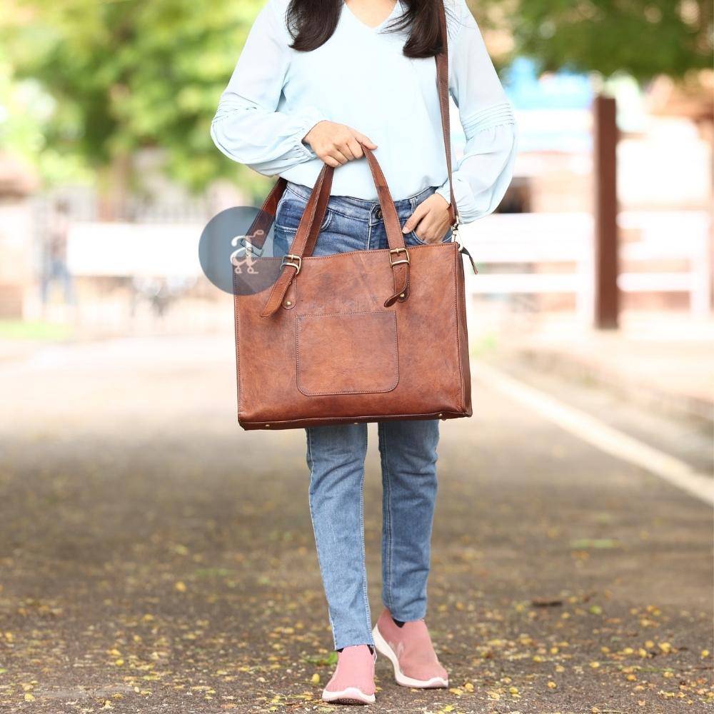 Woman Walking on a Leaf-Covered Path Carrying the Leather Laptop Tote Bag with Brass Buckles and Front Pocket