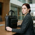 Woman seated at a boardroom table with The Virtuoso black leather briefcase standing on end beside her