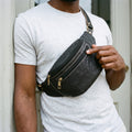 Man wearing a black leather fanny pack across his chest, showing the white contrast stitching and brass zips