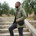 Man in an olive jacket climbing stone steps with a black leather fanny pack worn as a sling