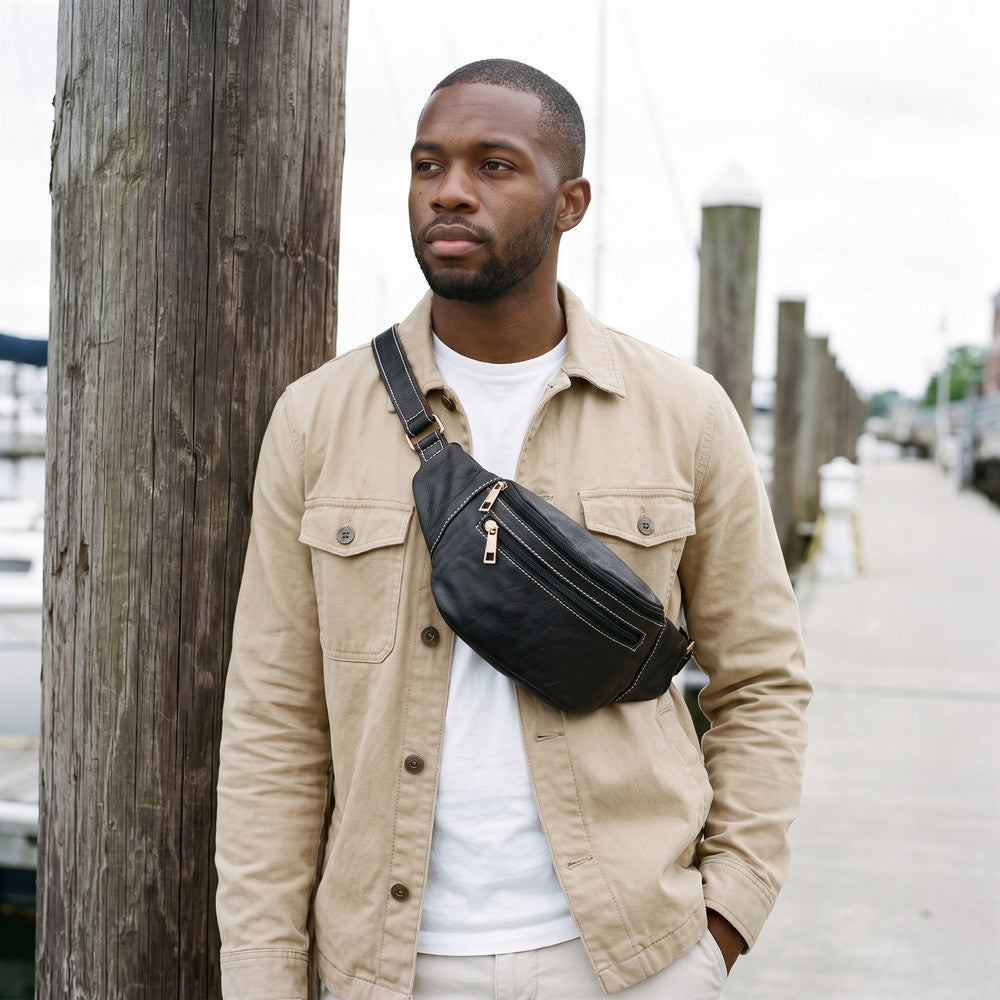 Man in a beige jacket wearing a black leather fanny pack across his chest on a harbour boardwalk