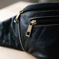 Close-up of the brass zip pulls and white stitching on a black leather fanny pack