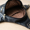 Close-up of the open main compartment of a black leather fanny pack with brown chevron lining