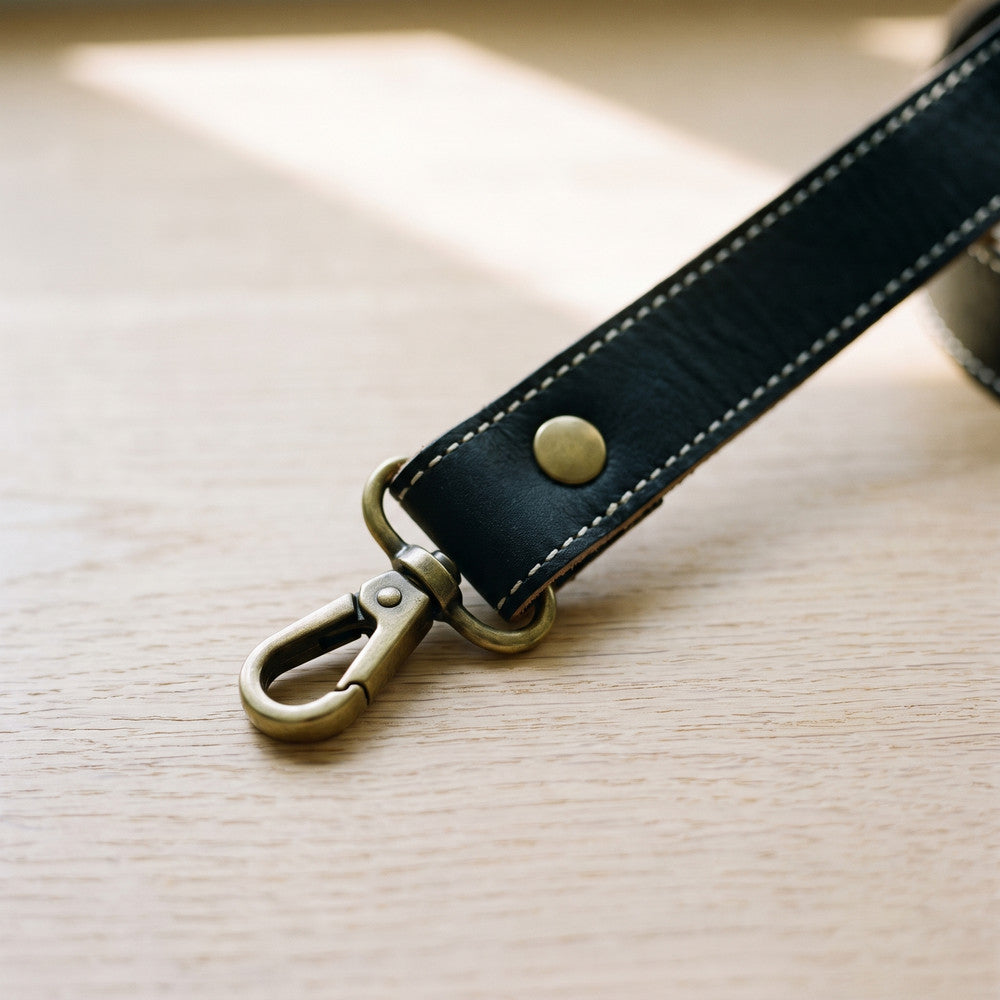 Close-up of the black leather strap with a brass snap hook and stud