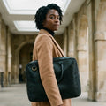 Woman in a camel coat holding The Specialist black leather laptop briefcase under her arm in an arched atrium