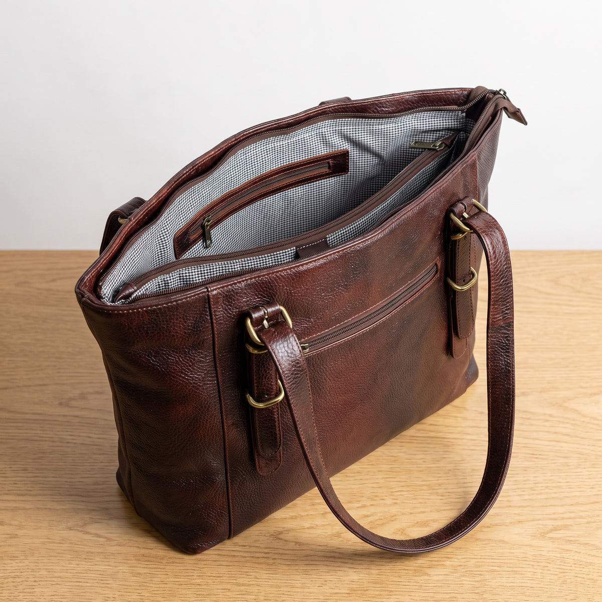 Open dark brown leather purse on a wooden table showing the grey lining and inner zip pocket