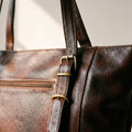Close-up of the brass buckles, pebbled leather and front zip pocket on the dark brown leather purse