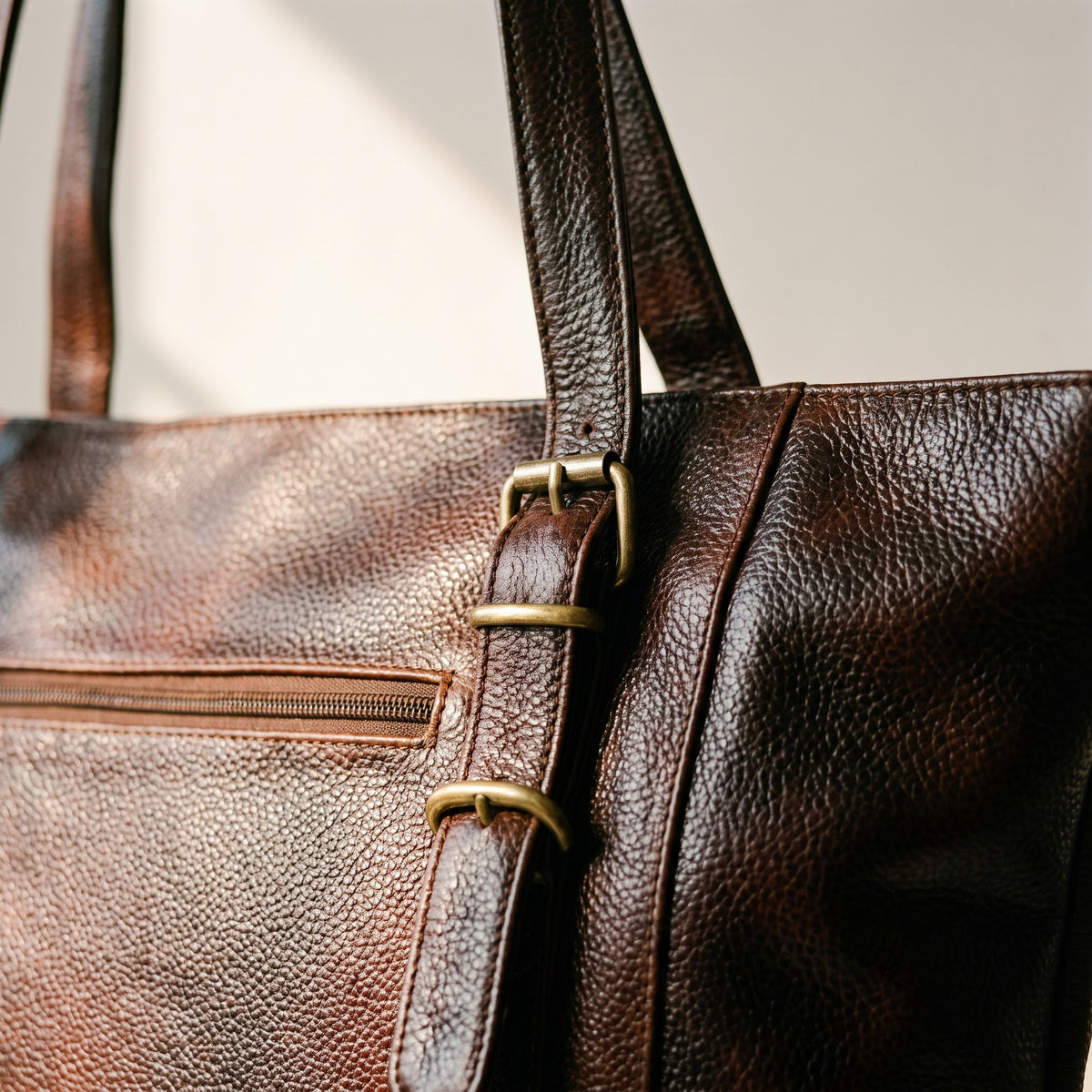 Close-up of the brass buckles, pebbled leather and front zip pocket on the dark brown leather purse