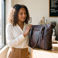 Woman in a cream blouse in a cafe resting her hand on the dark brown leather purse