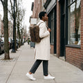 Side profile of The Convertible leather backpack worn on both shoulders on a shopping street