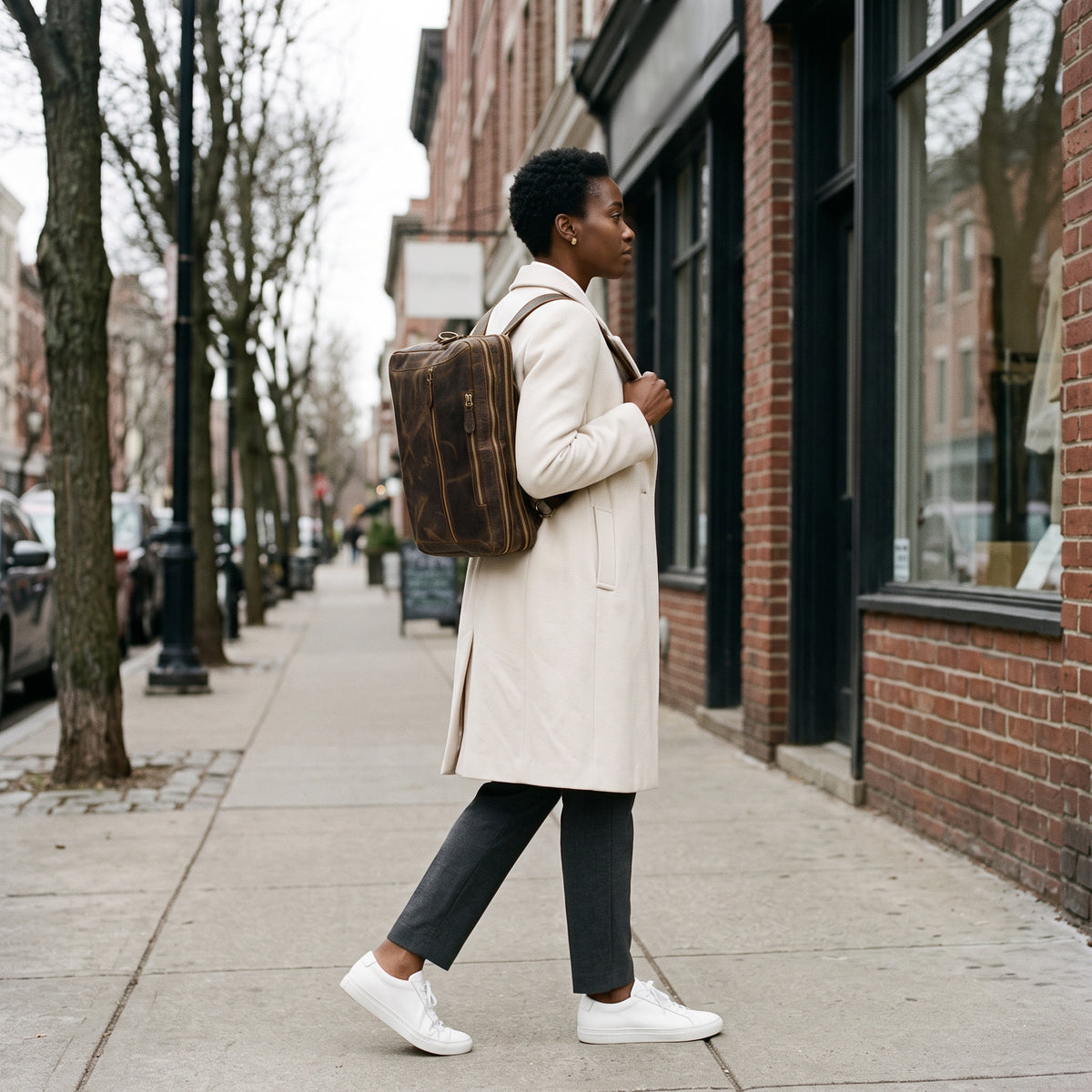 Side profile of The Convertible leather backpack worn on both shoulders on a shopping street