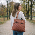 Back view of a woman on a park path carrying the quilted brown leather designer tote bag, showing its back zip pocket