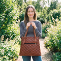 Woman in a striped top holding the quilted brown leather designer tote bag by its handles on a garden path