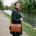 Man on a canal towpath wearing The Executive tan leather briefcase crossbody on its shoulder strap
