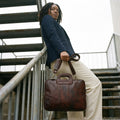 Woman in a navy blazer on an outdoor staircase holding The Negotiator leather laptop briefcase by its shoulder strap