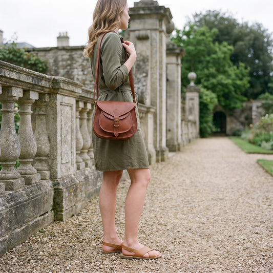 Woman in an olive dress on a garden path carrying the tan leather crossbody purse on her shoulder
