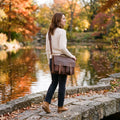 Woman on a lakeside path in autumn wearing The Digital leather laptop messenger bag crossbody