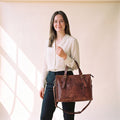 Woman in a cream blouse carrying the Anuent brown leather laptop tote bag on her shoulder