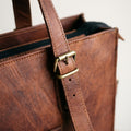 Close-up of the brass buckle and stitched leather handle on the brown leather laptop tote bag