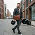 Man wearing The Cruiser leather motorcycle bag crossbody on a city street with his helmet in hand