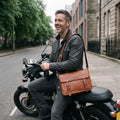 Rider seated on a motorcycle pulling on gloves with The Cruiser leather bag worn crossbody