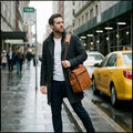 Man at a taxi rank wearing The Navigator leather messenger bag on his shoulder, showing the back zip pocket