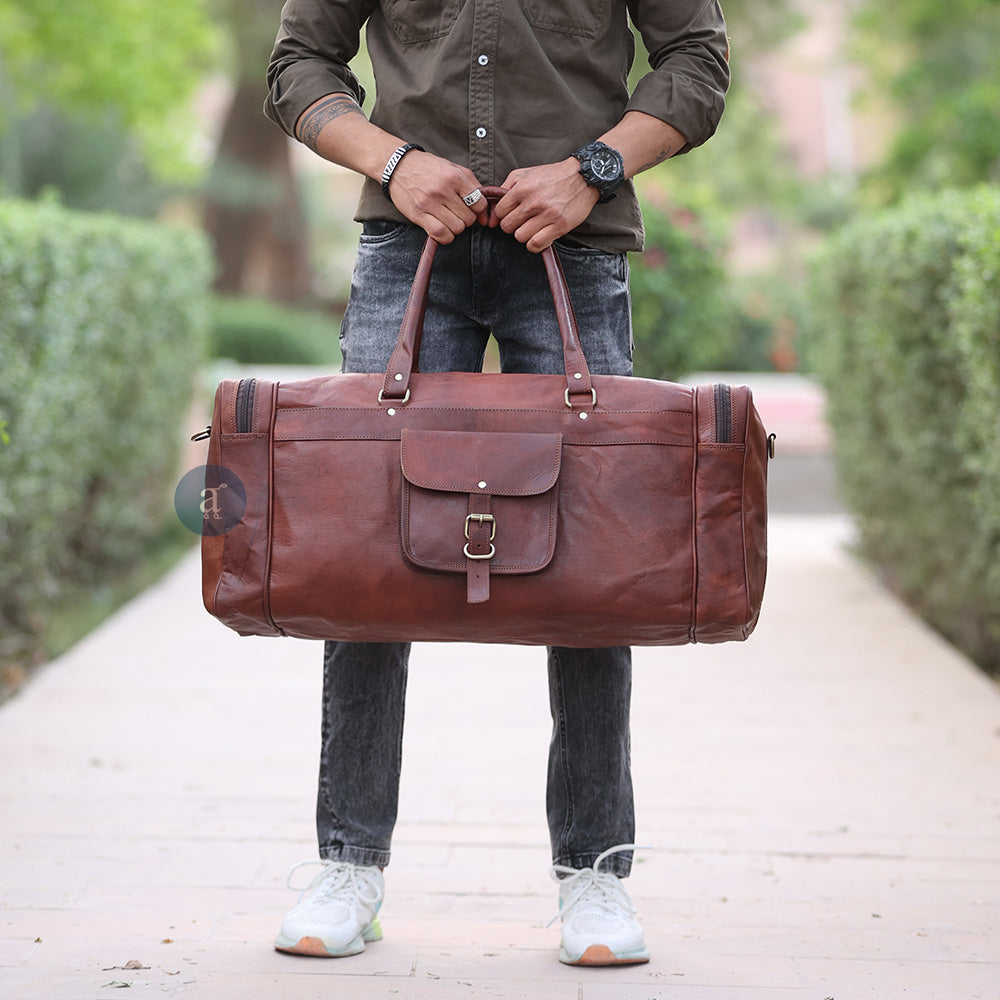 A Man Holding The Yachtsman Duffle In Hand, Wearing A Brown Shirt And Jeans, Standing On A Pathway